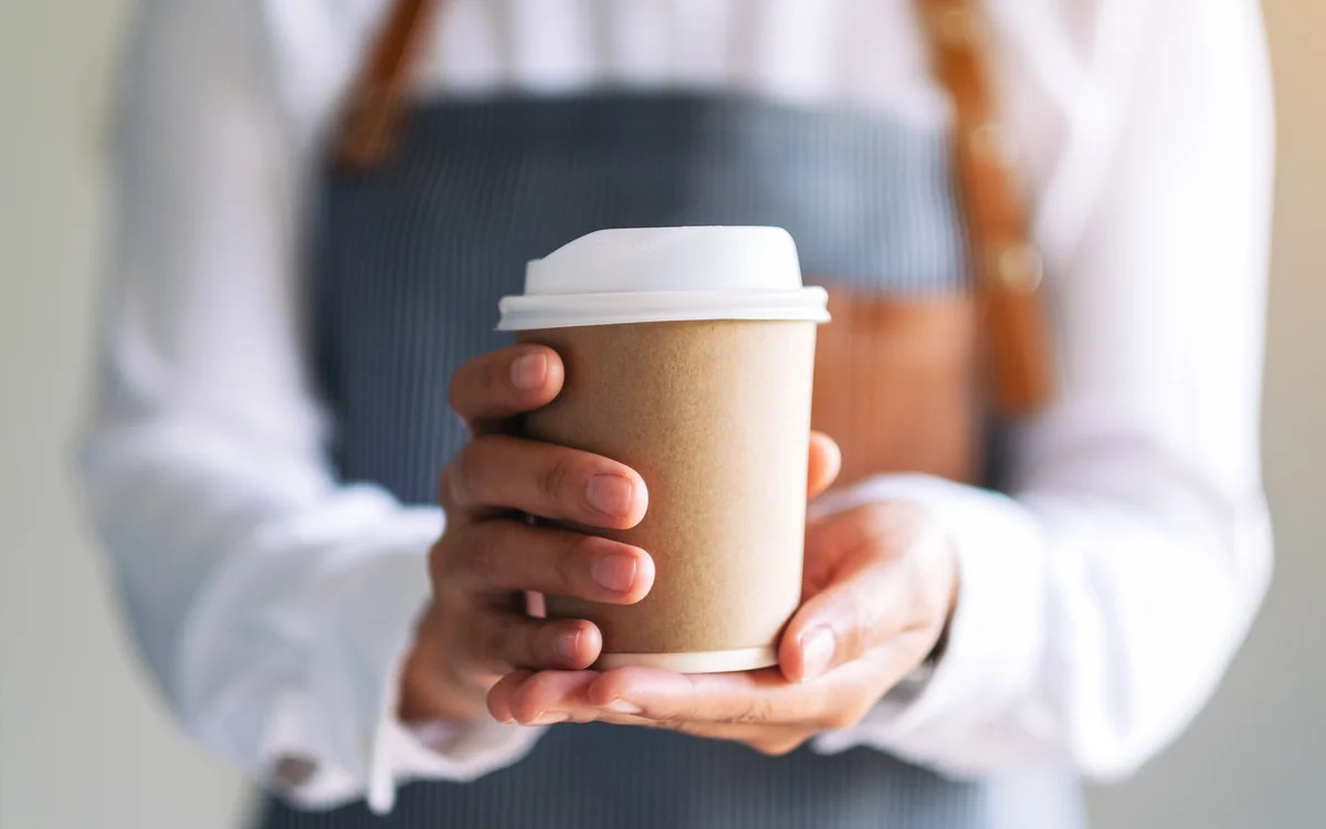 テイクアウト用のカップに入ったコーヒーを両手で差し出すスタッフ